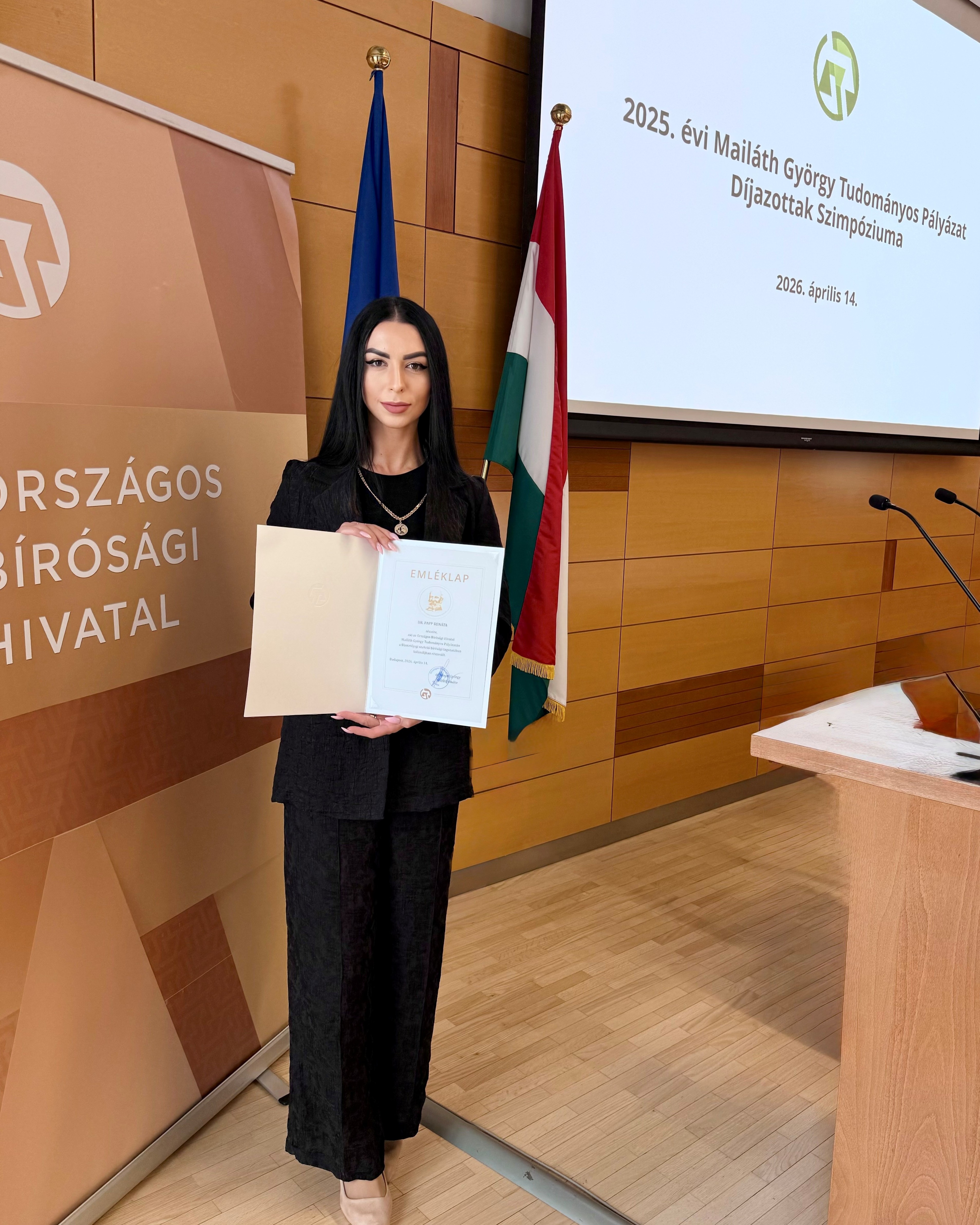 A képen Papp Renáta a KRE ÁJK Doktori Iskola hallgatója látható, ahogyan tartja az oklevelét a Mailáth György Tudományos Pályázat díjátadóján.